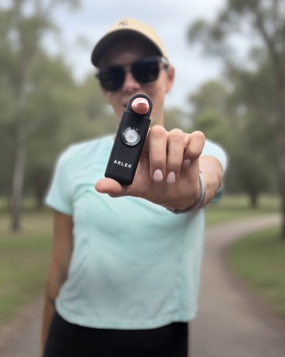 Woman holding ARLEK Black Edition personal safety alarm ready to activate during run